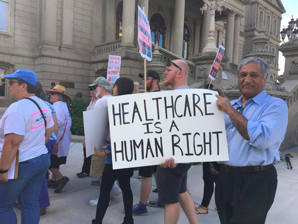 Dr Kumar protesting with sign that says Healthcare is a Human Right